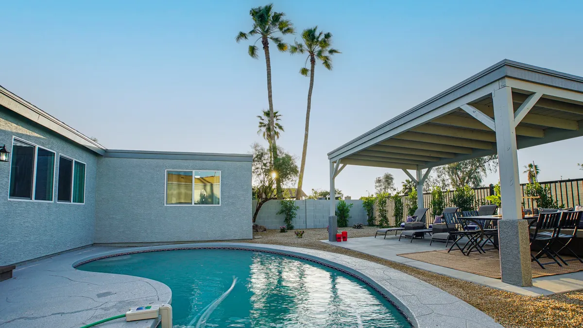 A sparkling swimming pool sits at the center, flanked by a covered patio and tall palm trees. The inviting poolside area is perfect for post-golf relaxation, while the lush greenery and ample outdoor seating create an atmosphere of leisure and comfort under the Arizona sky.
