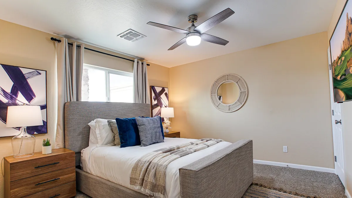 A cozy bedroom with a comfortable bed, nightstands, and elegant artwork. Soft lighting creates a warm, inviting vibe, and sunlight filters through, enhancing the peaceful ambiance.