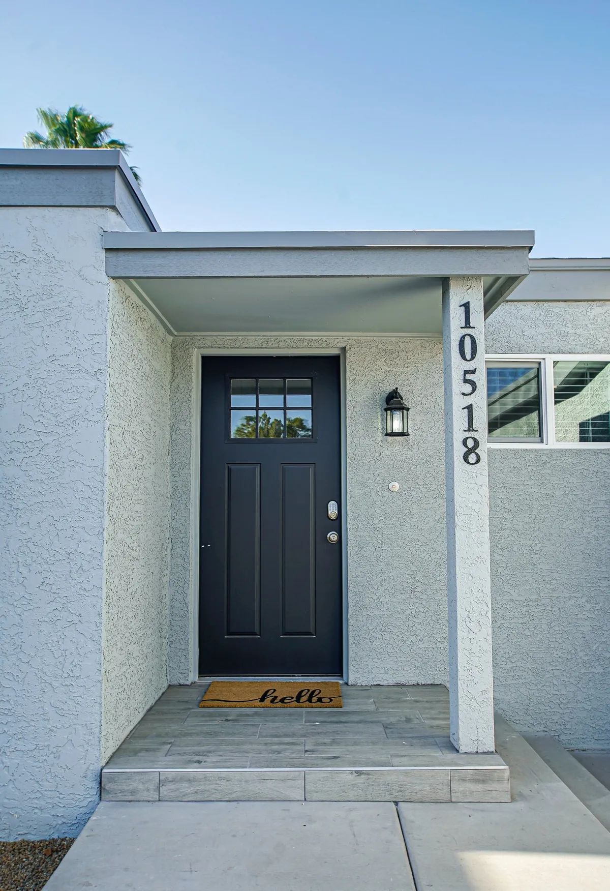 A bright exterior shot of the home's entrance with a prominent black front door, a welcoming mat, and clear house number, suggesting easy, friendly arrivals—including for guests with pets.