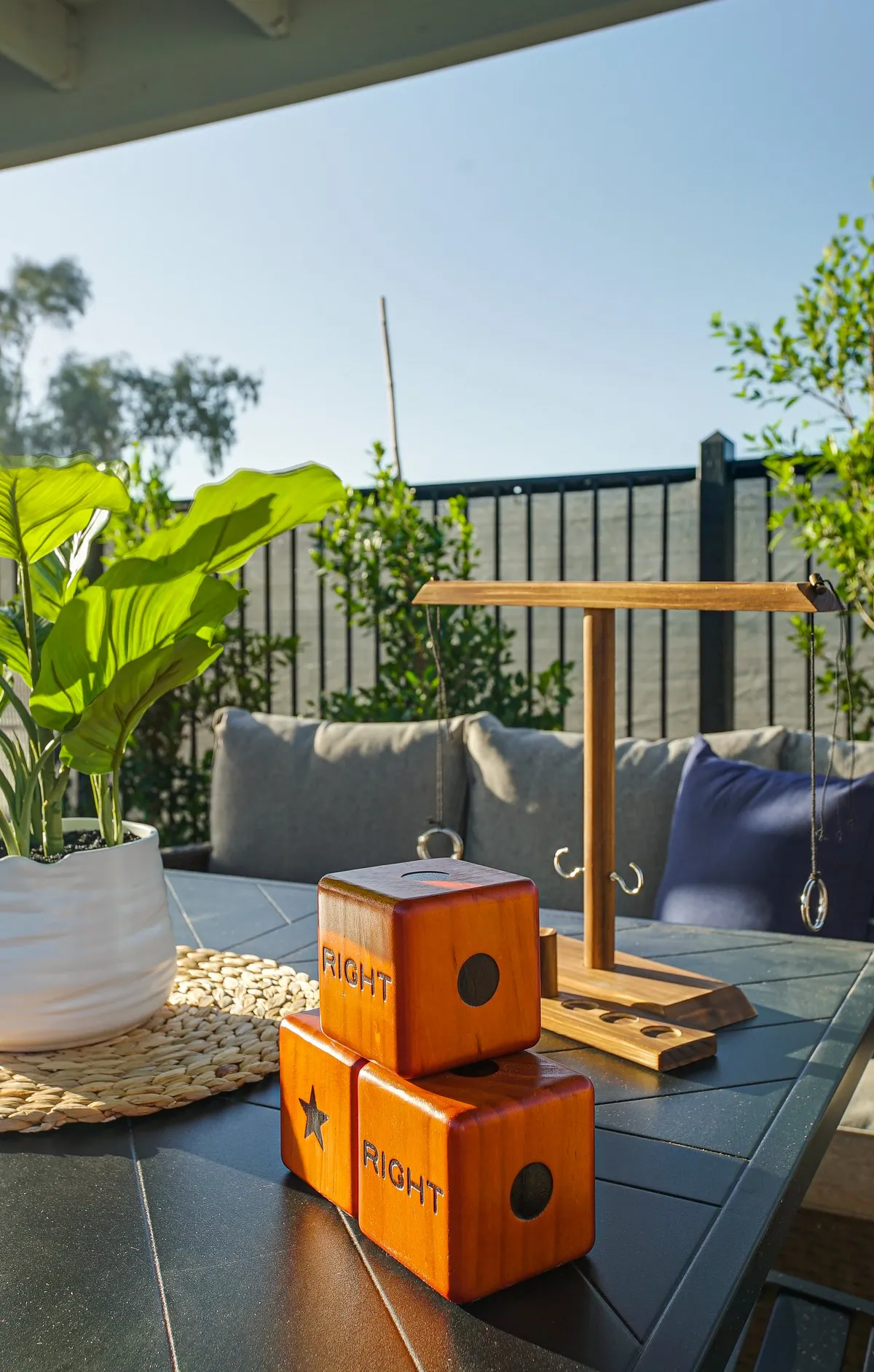 A playful outdoor tabletop scene with wooden blocks engraved with 'RIGHT', a potted green plant, and a textured table surface—suggesting space for games, casual dining, and relaxed group activities in the fresh air.
