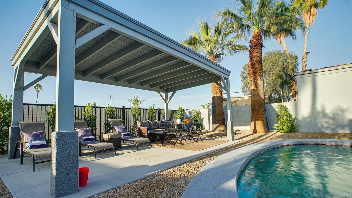 This image presents a view of the backyard featuring the private swimming pool surrounded by outdoor seating, palm trees, and a dining table. The setup conveys a relaxing, inviting atmosphere ideal for both swimming and outdoor gatherings.