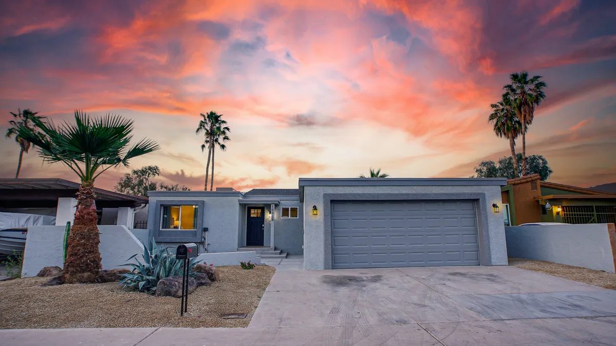 This exterior image features the vibrant front of the property with tall palm trees, a sleek modern garage door, and a beautifully landscaped yard set against a colorful sunset sky. The scene captures a welcoming entrance and the lively neighborhood atmosphere.