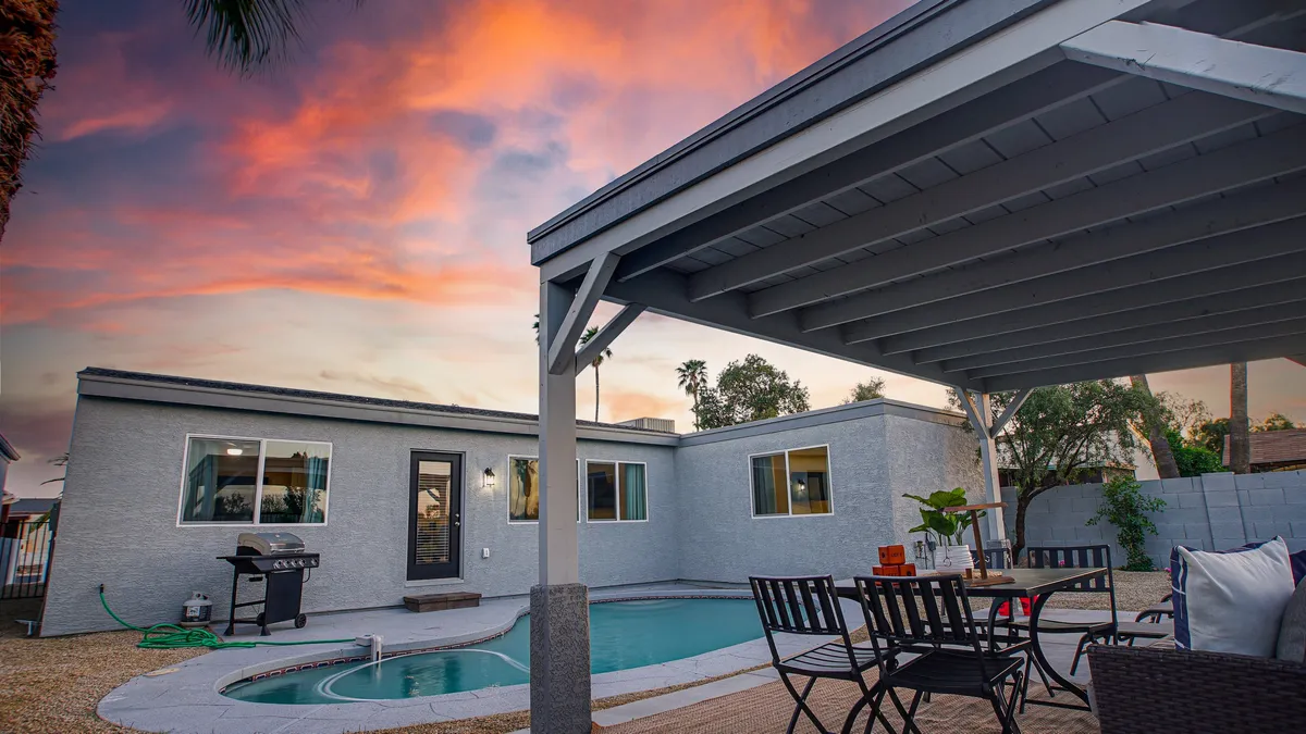 An elegant outdoor living area features a swimming pool surrounded by comfortable seating and a patio, all set against a dramatic sunset sky. The scene invites guests to gather for evening refreshments, enjoy cool dips in the pool, and take in tranquil views as the day winds down.