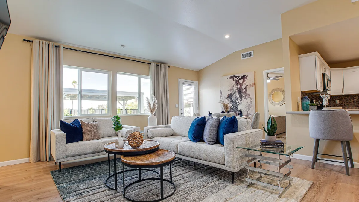 A cozy, sunlit living area featuring a sofa with decorative pillows, a stylish coffee table, cheerful artwork on the wall, and bright windows letting in natural light, creating a welcoming ambiance for guests and their pets.