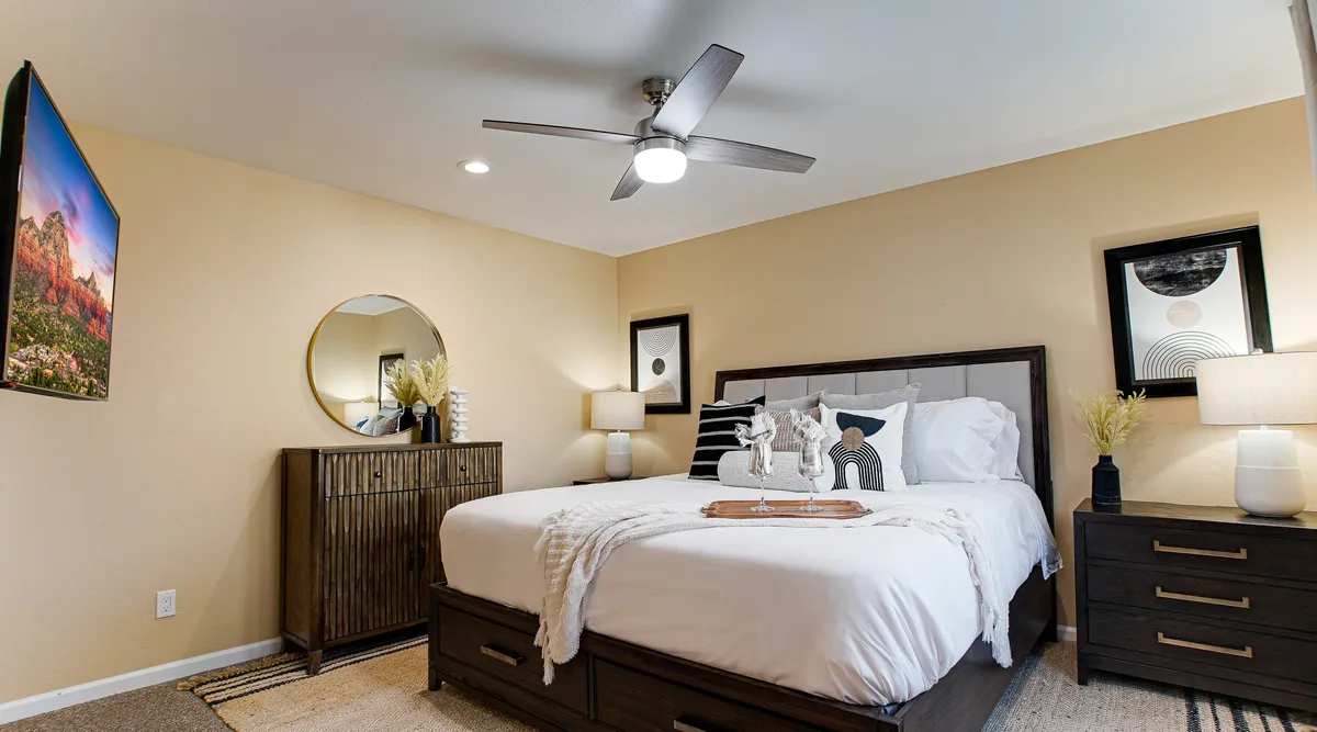 A tranquil bedroom featuring a king-sized bed adorned with decorative pillows, stylish bedside lamps, and contemporary artwork on the walls. A circular mirror adds a touch of sophistication, while natural light streams in, creating a serene and inviting atmosphere.