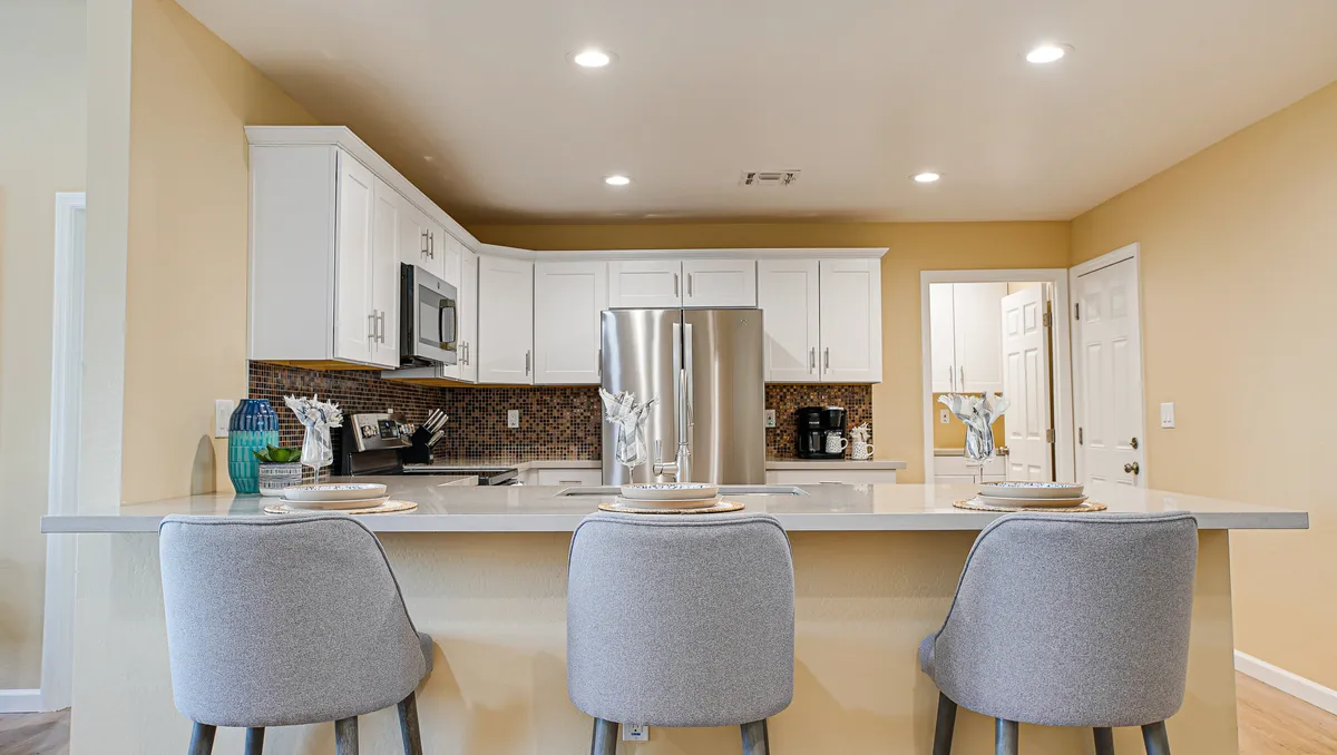 A modern kitchen is showcased with a sleek island, stainless steel refrigerator, and a pair of bar stools. The friendly, approachable layout is designed for cooking, entertaining, and sharing casual meals, with ample light and contemporary finishes.