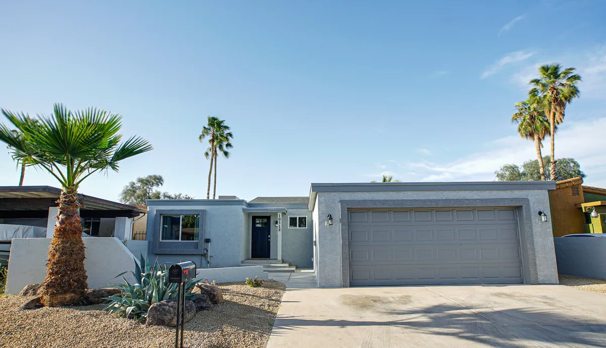 A view of the home's front entrance framed by palm trees, landscaped gravel areas, and a welcoming porch. The sunny Arizona sky and greenery highlight the inviting exterior and the sense of open space.