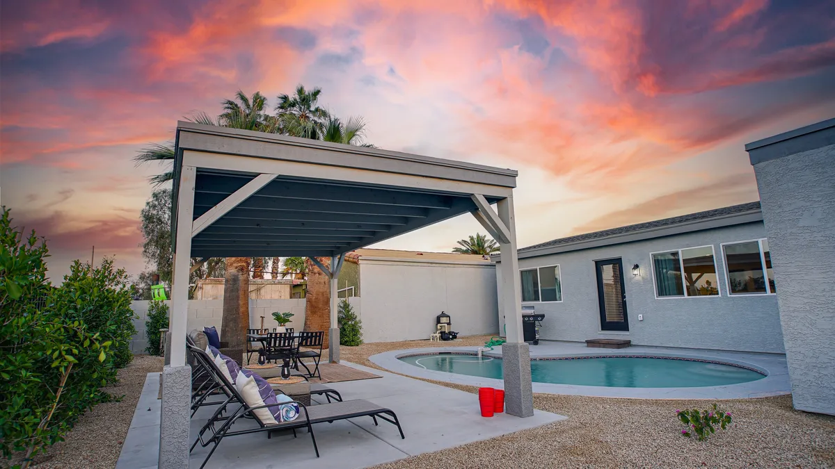 A tranquil backyard scene featuring a sparkling swimming pool, outdoor seating area, and a vibrant sunset sky. The setup is tailored for relaxation, with space for lounging and playing outdoors.