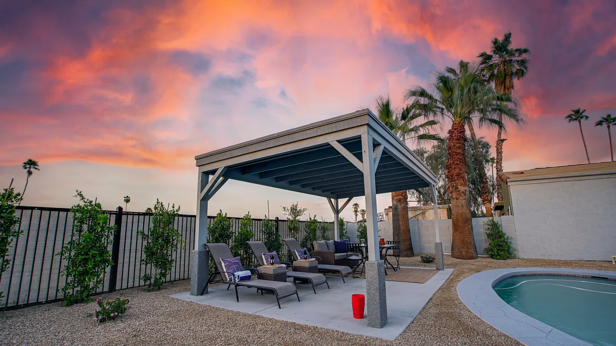 A resort-style backyard is the focal point here, with a sparkling swimming pool, shaded pergola, lounge chairs, and tall palm trees under a vast sky. The inviting atmosphere suggests opportunities for pre-game relaxation or post-event celebrations with friends.